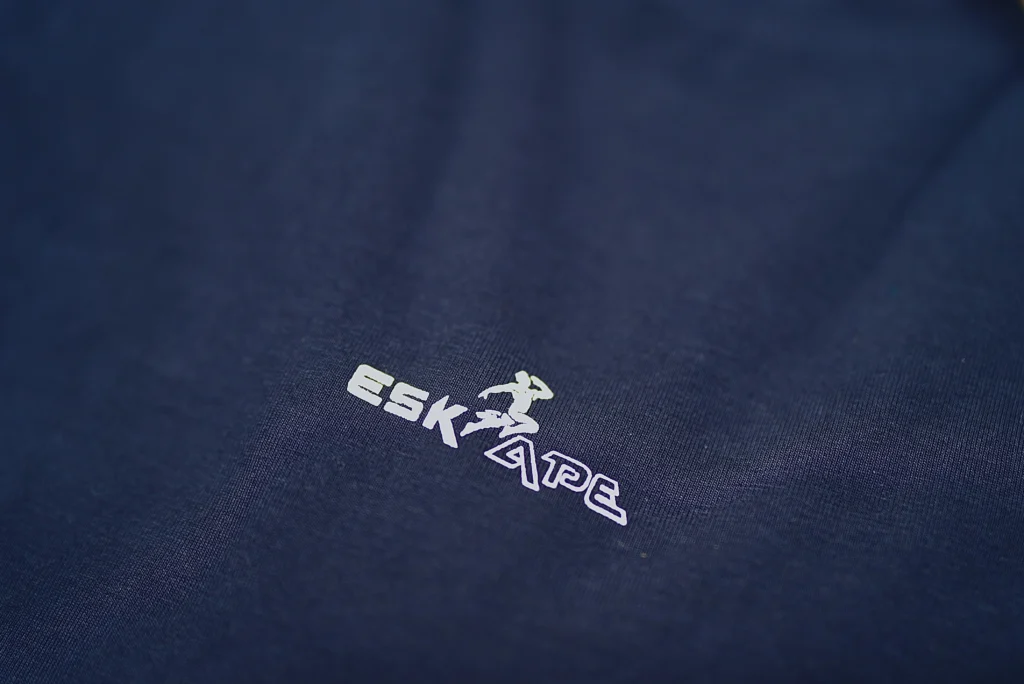 A close-up shot of the ESKAPE logo embroidery on a navy blue oversized drop-shoulder t-shirt, highlighting the premium fabric texture and minimalistic branding. The sleek and modern logo represents ESKAPE’s luxury streetwear identity.